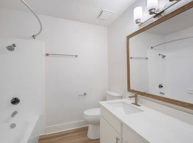 Bathroom with white countertop, large mirror, wood style flooring, toilet, and brushed nickel fixtures